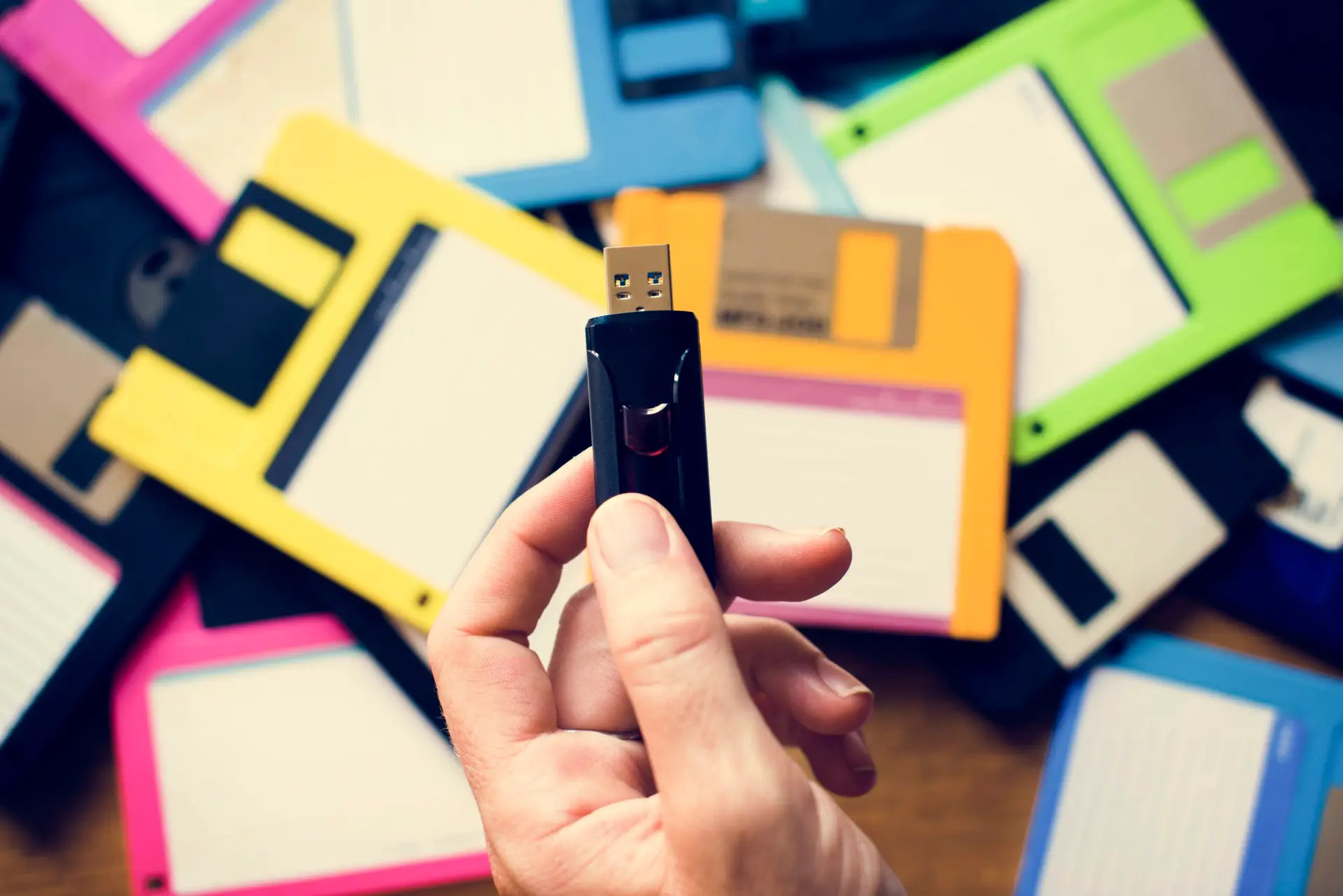 Someone holding thumbdrive over a pile of floppy disks